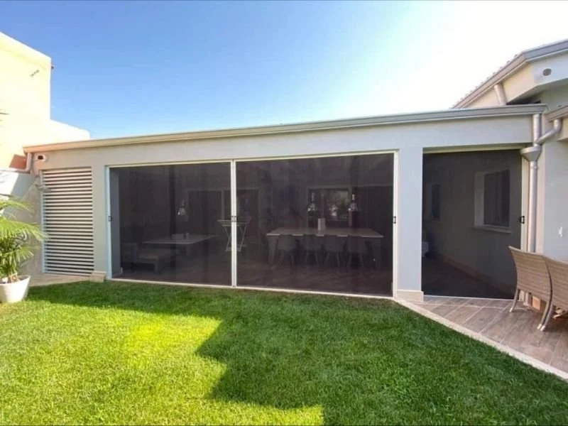 Moustiquaire plissée installée sur une baie vitrée donnant sur une terrasse et un jardin ensoleillé.