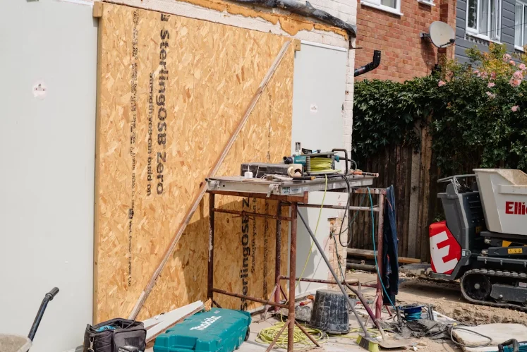 Chantier de rénovation énergétique sur une maison mitoyenne avec panneaux OSB, échafaudage et outils de construction en extérieur.